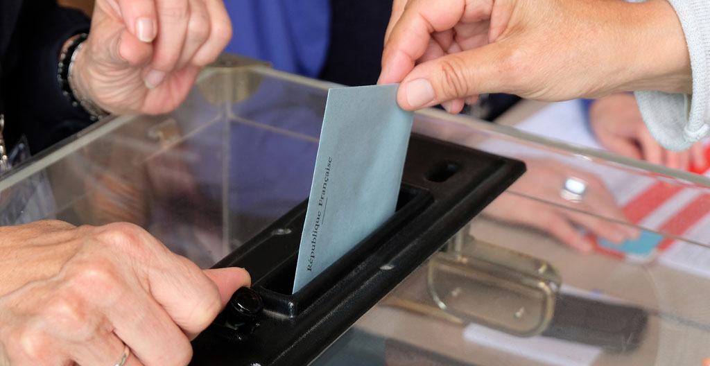 Salle de vote aménagée en entreprise française avec urne transparente scellée, isoloir déployé, bulletins de vote et affiches électorales réglementaires affichées en préparation du scrutin CSE